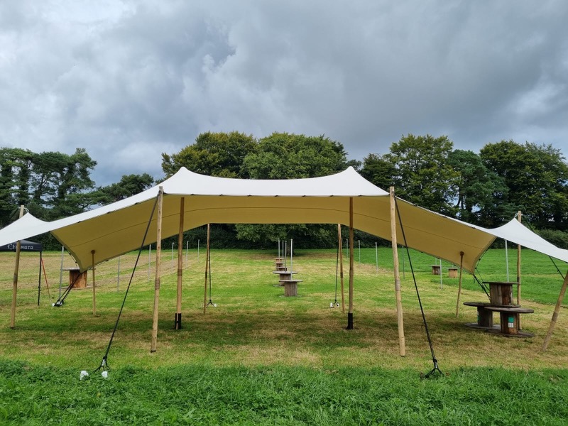 StretchScape stretch tent installed in an open field with rustic cable-spool tables for a private outdoor celebration